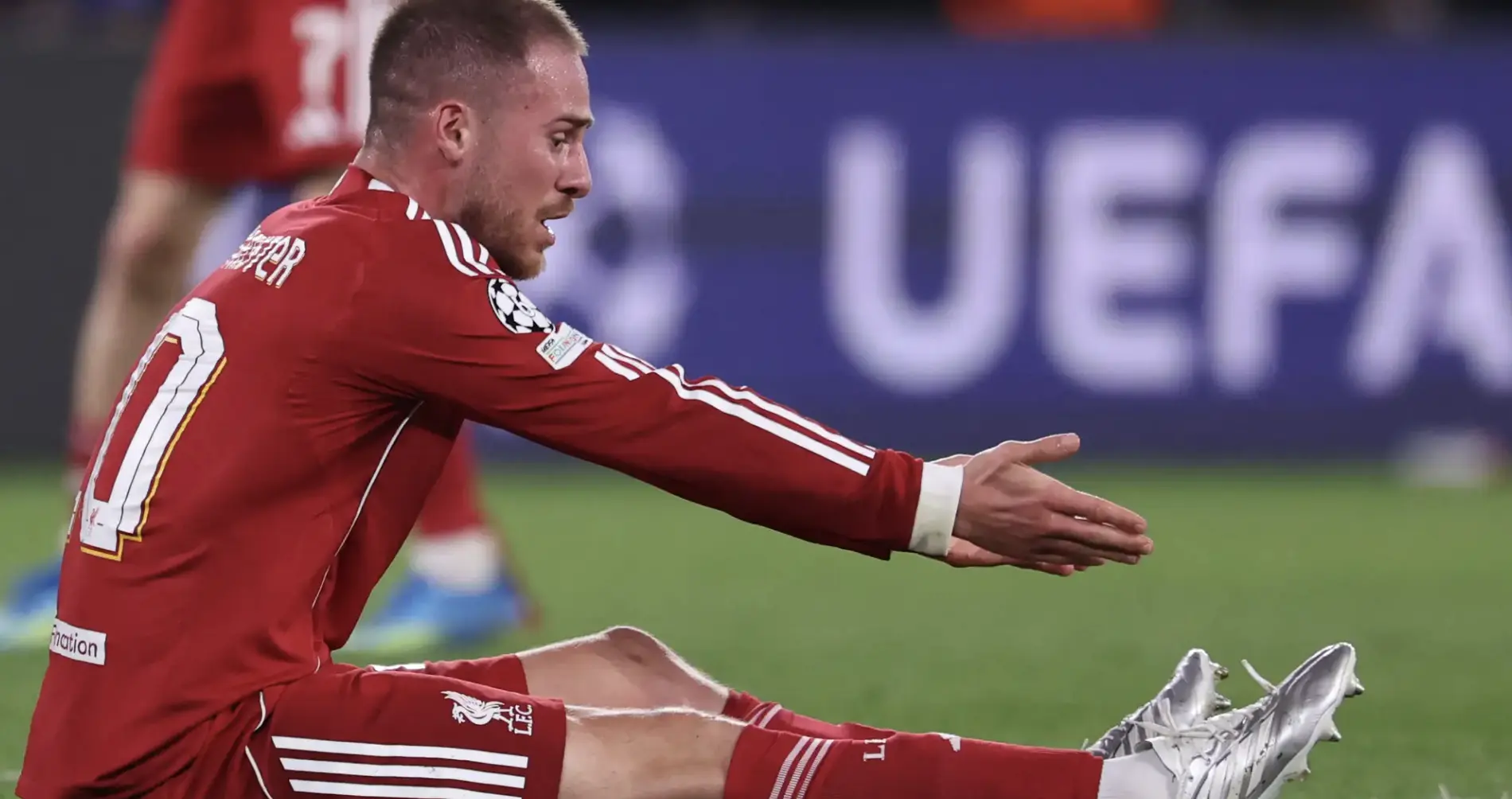 Liverpool footballer in red kit extending leg to kick the ball during a match, stadium blurred in the background, action shot.