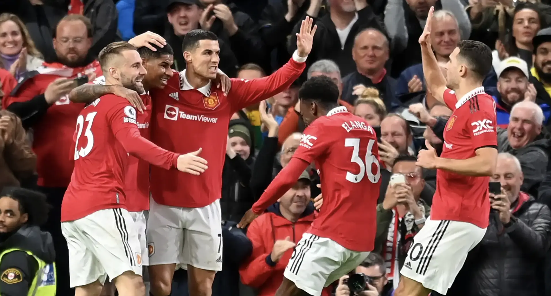 Manchester United players in red kits celebrate a goal with arms raised as fans cheer in the background