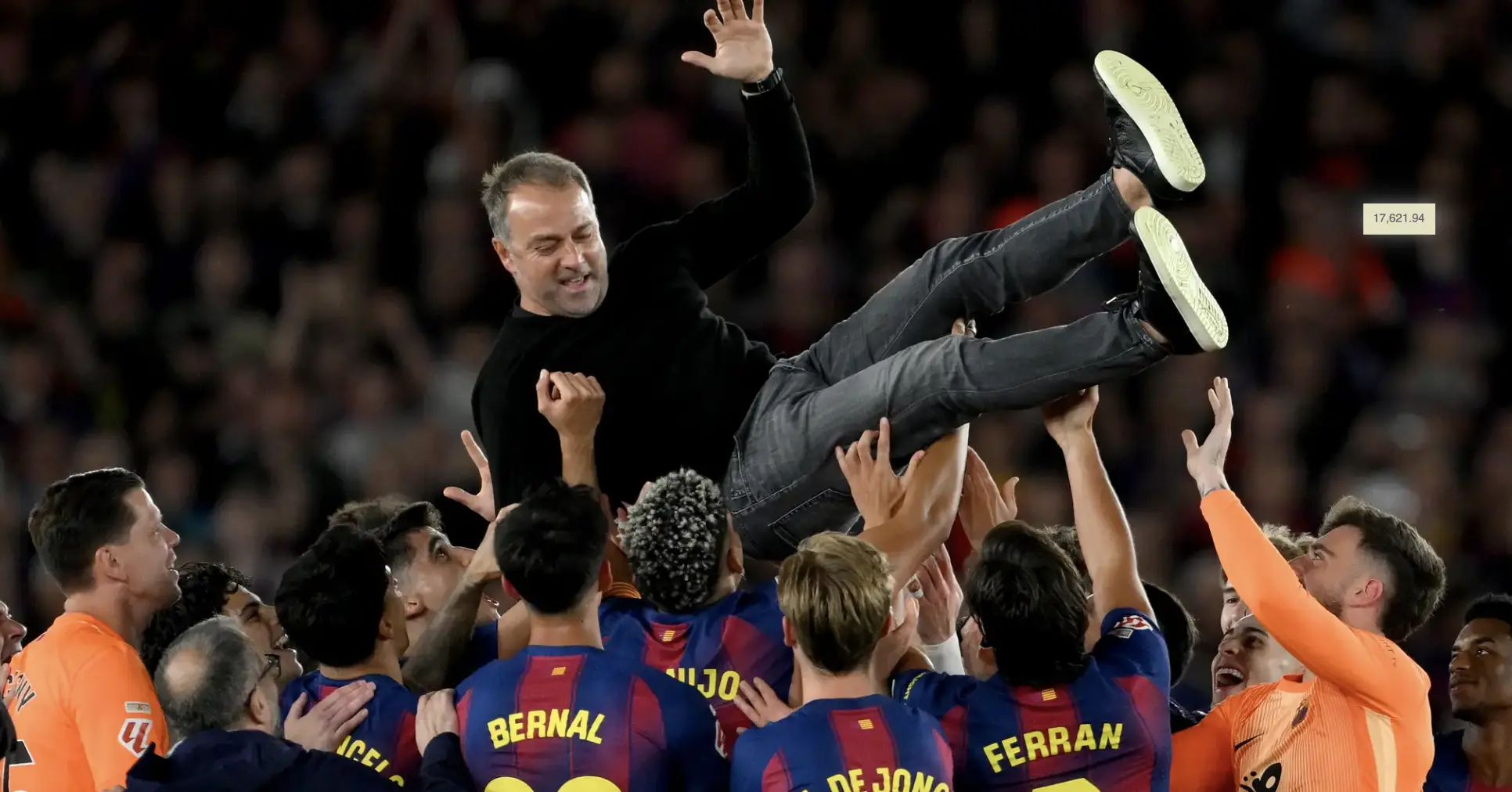 A man is lifted above a cheering crowd by teammates in a stadium, celebrating a win.