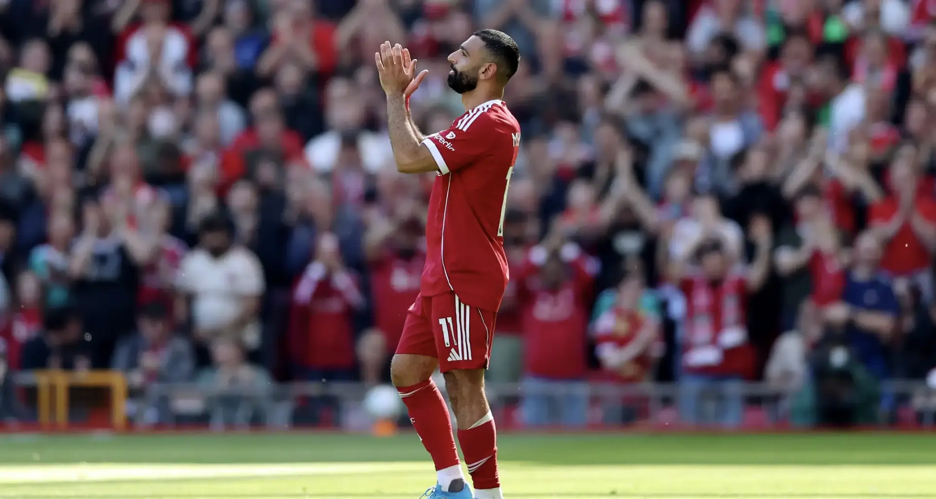 Soccer player in red kit claps on the pitch as a cheering crowd looks on.