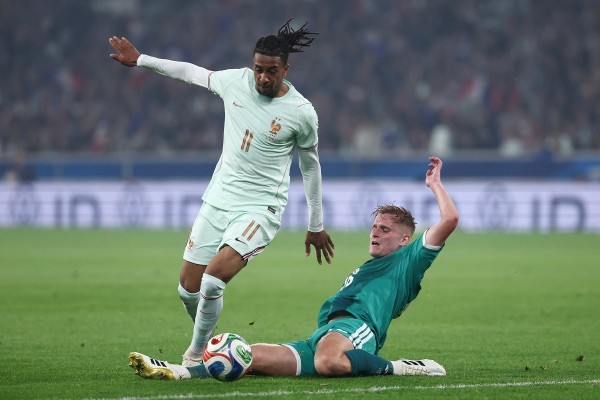 Soccer match moment as a mint-jersey attacker controls the ball while a teal-kit defender slides in to challenge.