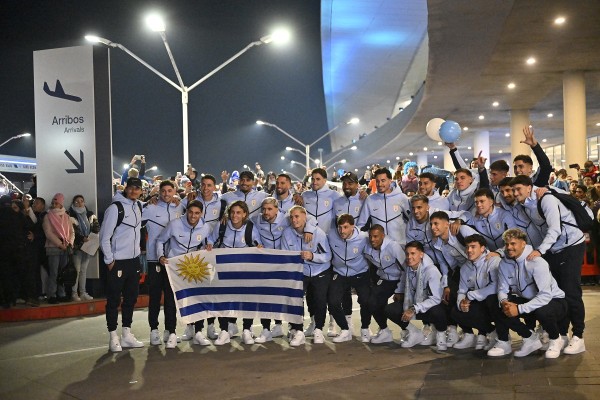 39653650461_600x400 - 實發體育 Group of athletes in light-blue jackets posing with the Uruguay flag at a night-time airport arrivals area.