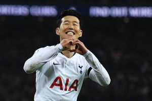 8gyZVJbb9EJvXKrCovAnwtilUs3h44y2Z0X6MmdF-jI - 實發體育 Tottenham Hotspur player in a white jersey making a heart gesture with his hands during a match, stadium lights in the background.