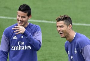 Two male soccer players in Real Madrid training gear laughing together on a green field.