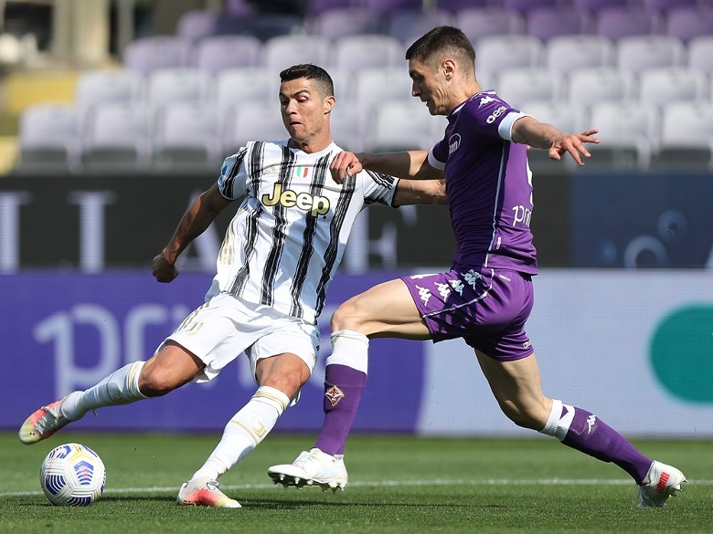 Two soccer players in a tackle for the ball during a match; one in Juventus striped kit, the other in Fiorentina purple kit.