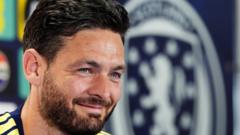 Close-up of a man with dark hair and beard, smiling, with a Chelsea FC emblem visible in the background
