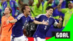 Two soccer players in blue celebrate a goal as fans cheer in the background.