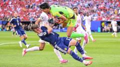 cover-8056-1781920830jpg - 實發體育 Soccer player in a white jersey and navy shorts dribbles with the ball while a neon-green goalkeeper tensions in to challenge him; stands full of fans in the background.