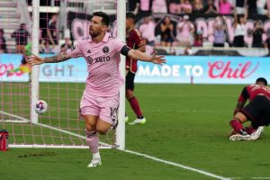 Soccer player in a pink kit celebrates with arms outstretched near the goal after scoring