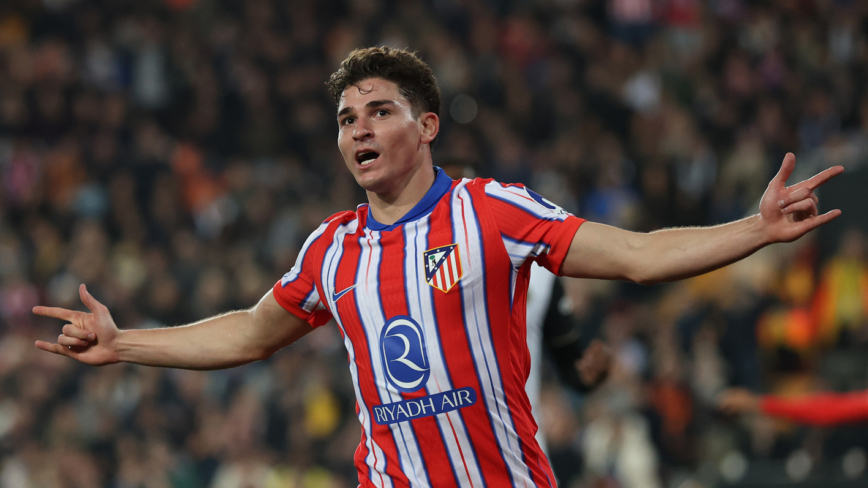 Valencia CF v Atletico de Madrid - La Liga EA Sports - 實發體育 Soccer player in a red-and-white striped jersey celebrates with arms wide open on the field during a match, crowd in the background.
