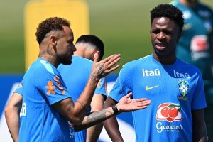 Two Brazilian football players in blue training jerseys high-fiving during practice on a sunny day.