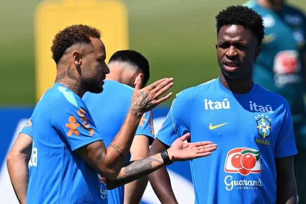 Two Brazilian football players in blue training jerseys high-fiving during practice on a sunny day.