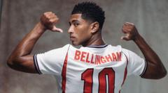 Soccer player shown from the back in a white jersey with 'Bellingham' and the number 10, flexing both arms overhead.