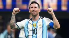 Lionel Messi in the Argentina jersey raises his fists in celebration on the pitch after a goal.