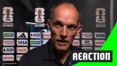 Close-up of a man speaking at a sports press conference, sponsor logos in the background, with a bright green 'REACTION' badge.