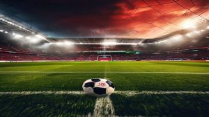 cover-8857-1784509236jpg - 實發體育 Soccer ball resting on the green pitch at the edge of the field with a large, illuminated stadium and a red-orange sunset sky in the background as floodlights glow overhead.