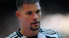 Close-up of a young man with short dark hair and a trimmed beard wearing a black-and-white striped sports jersey, looking off to the side.
