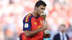 cover-9022-1785031220jpg - 實發體育 Soccer player in a red jersey kissing a gold trophy during a stadium celebration.
