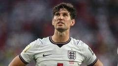 cover-9067-1785456058jpg - 實發體育 English footballer in a white England jersey on the pitch, hands on hips, looking into the distance.