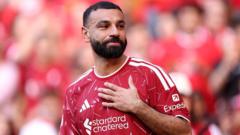 Liverpool footballer in a red jersey celebrates with a hand on his chest on the pitch.