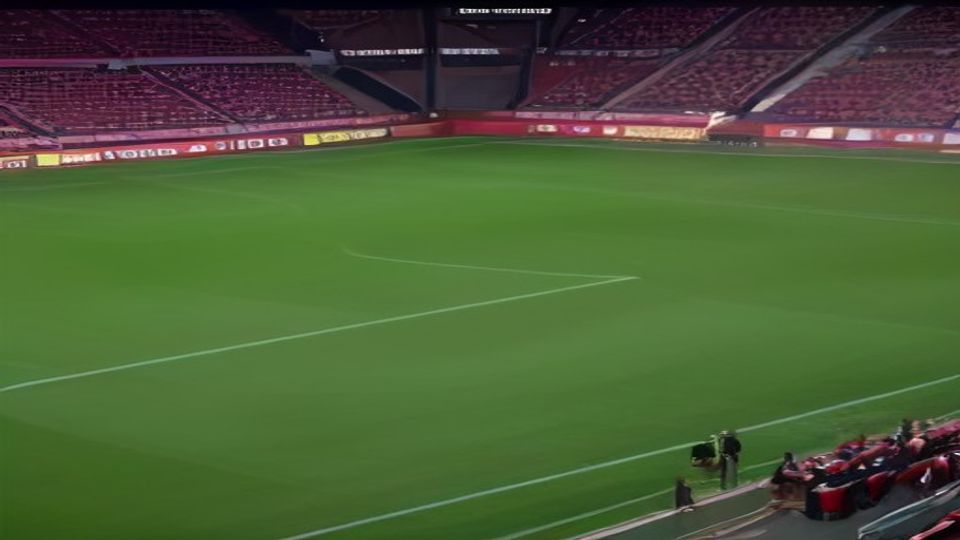 cover-9139-1785974458jpg - 實發體育 A green soccer field inside a stadium with red seats; few spectators and cameras near the sideline.