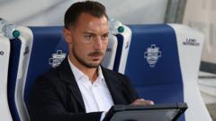 cover-9142-1785974464jpg - 實發體育 Man in a suit sitting in a stadium dugout, looking at a tablet.