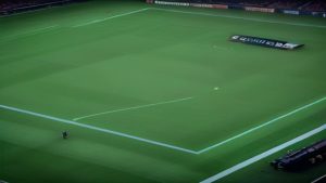 Aerial view of a lush green football pitch with players or staff near the sideline and a banner on the field edge.