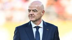 Bald man in a dark suit and blue tie, looking to the left, outdoors with a blurred crowd in the background.