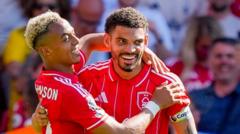 Two soccer players in red jerseys celebrate a goal, embracing and smiling on the field.