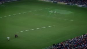 cover-9230-1786669231jpg - 實發體育 Aerial view of a soccer stadium with players walking across the green field toward the left while spectators fill the stands behind them, near a goal area in the distance.
