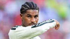cover-9245-1786838458jpg - 實發體育 Close-up of a footballer with braided hair in a white jersey raising his arm on the field.