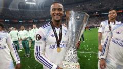 Real Madrid players celebrate on the field, with a player holding a large silver trophy in front of teammates.