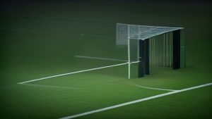 cover-9326-1787446827jpg - 實發體育 Soccer field at night with a metal goal and net, and a dark tunnel-like structure behind it on green turf.