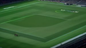 cover-9462-1788742830jpg - 實發體育 Aerial view of a large stadium with a freshly mowed field showing alternating green strips; two people walk near the bottom-left, logo visible on the pitch center-right.