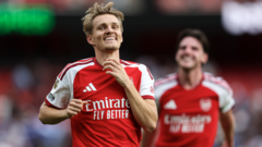 cover-9465-1788746423jpg - 實發體育 Two Arsenal players celebrate on the pitch in red jerseys, one raising his fist with a smile.